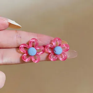 Gros plan de boucles d'oreilles fleurs rose et bleu tenues à la main pour le détail.