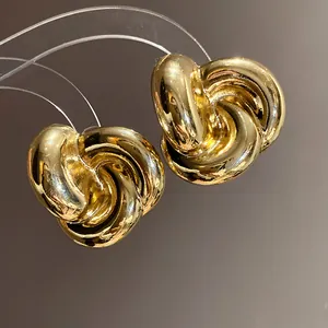 Primer plano de pendientes de botón dorados con diseño de nudo trenzado y acabado pulido