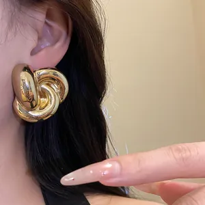 Primer plano de pendientes de flores retorcidas doradas de estilo vintage en la oreja