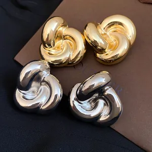 Primer plano de pendientes de flores retorcidas en color oro y plata de estilo vintage.
