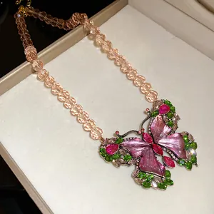 Macro view of vintage butterfly pendant necklace with pink enamel and green gems
