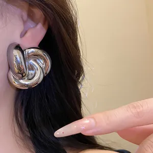 Primer plano de un elegante pendiente de botón con nudo retorcido plateado en oreja