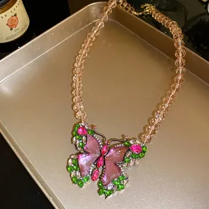 Close-up of a vintage butterfly necklace with pink resin wings and rhinestones on a gold tray.