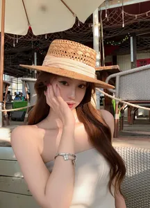 Elegant young woman in a straw hat wearing a stylish designer clover charm bracelet at a sunlit cafe