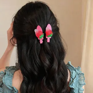 Détail de deux jolies barrettes fraises portées sur de longs cheveux foncés ondulés.