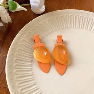 Gros plan de barrettes à cheveux orange en forme de fruit sur une assiette en céramique.
