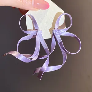 Primo piano di eleganti orecchini a fiocco in nastro di raso viola con trama setosa.
