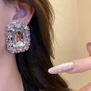 Close-up of a large square silver stud earring with clear sparkling rhinestones on ear.