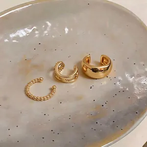 Set of three elegant gold-plated ear cuffs with zircon accents on a textured plate