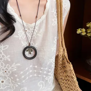 Vintage wooden ring necklace with leaf pendant worn on a white embroidered top.