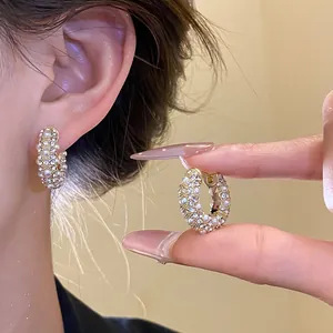 Detailansicht eleganter goldener Creolen mit funkelnden Strasssteinen und weißen Perlen