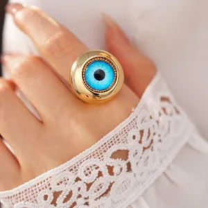 Audace anello occhio del diavolo dorato con iride blu su dito e pizzo bianco.