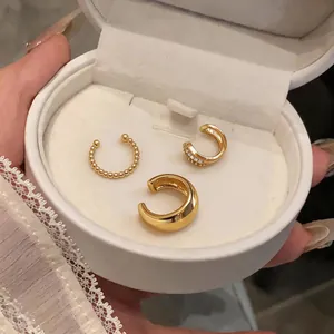 Detailed close-up of three gold-plated zircon ear cuffs inside a white jewelry box.
