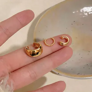 Close-up detail of three elegant gold-plated ear cuffs in various styles held on fingers.