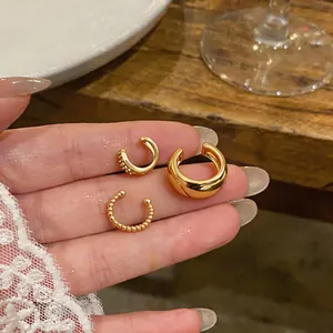 Close-up view of three gold ear cuffs held on fingertips showcasing minimalist design