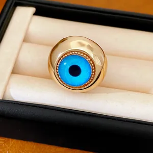 Primo piano di un anello in resina dorata con motivo occhio greco blu in un astuccio.