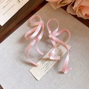Vista macro dei dettagli di orecchini a fiocco in nastro di seta rosa su carta.