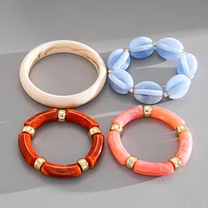 Close-up of four marbled acrylic bracelets with gold spacers on a grey textured surface