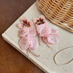 Detail view of pink chiffon flower tassel earrings placed on a vintage book background