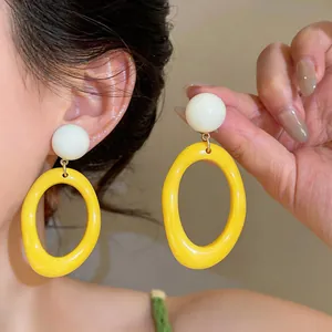 Close-up showing the glossy texture of yellow resin oval hoop earrings with a white ball