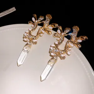 Dettaglio di orecchini retrò dorati con strass, smalto bianco e pendenti in cristallo.