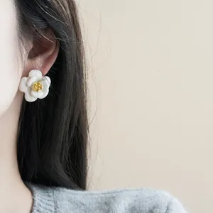 Detailed shot of elegant milky white camellia flower earrings with golden center on model