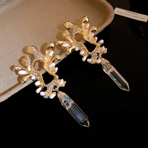Dettaglio di orecchini pendenti dorati con strass, smalto bianco e pendenti in cristallo