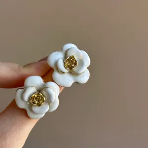 Close-up of elegant French-style white enamel flower earrings with gold rose center