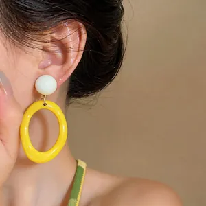 Close-up detailed view of vibrant yellow resin oval earrings worn by an Asian model