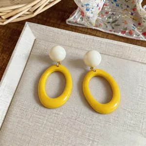 Close-up of vibrant yellow and white resin oval drop earrings on textured background