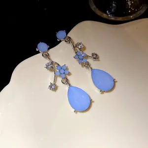Close-up of silver-tone floral earrings with light blue teardrop resin pendants.