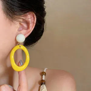 Close-up of yellow resin oval drop earrings worn by a model in soft light.