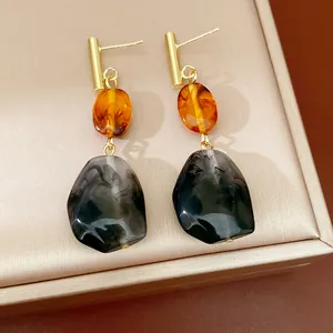 Primer plano detallado de pendientes de resina vintage con piedras ámbar y gris jaspeado