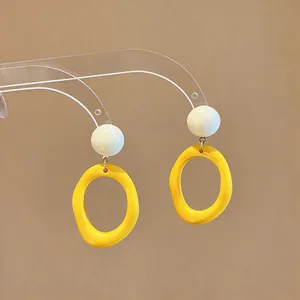 Close-up of yellow resin oval earrings with white stud on clear display stand.