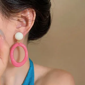 Close-up detail of stylish pink resin oval drop earrings worn by a fashion model