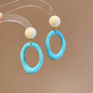 Close-up of blue resin oval earrings with white sphere stud on a transparent stand.