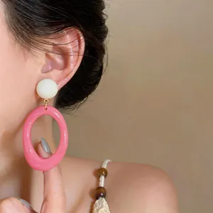 Detail view of pink resin oval earrings worn on the ear, showing size and style