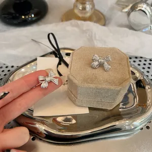 Close-up detail of sparkling silver zircon bow ear clips presented on a beige velvet jewelry box