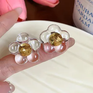 Close-up of clear resin flower stud earrings with yellow faceted rhinestone centers.