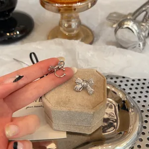 Detailed view of silver zircon-encrusted bow ear clips on a beige velvet jewelry box