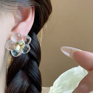 Close-up of transparent resin flower stud earring with yellow crystal on ear.