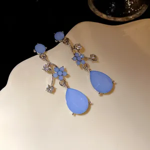 Close-up of elegant blue resin flower drop earrings with sparkling rhinestones on cream tray