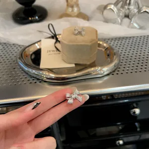 Close-up of a sparkling silver zircon bow-shaped ear clip held between fingers