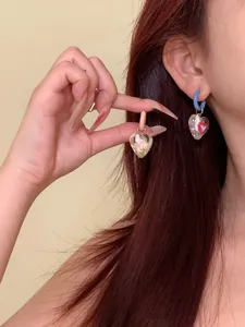 Detailed view of colorful asymmetric heart earrings with transparent charms on ear.