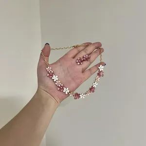 Handgehaltene Details zeigen das Schmuckset mit rosa-weißen Blumen und Ohrsteckern.