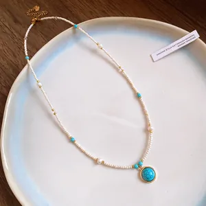 Close-up of vintage beaded necklace with a circular turquoise stone pendant on a white plate