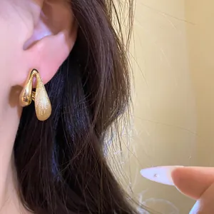 Primo piano di eleganti orecchini a goccia placcati in oro 18k con una trama spazzolata unica.