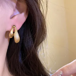 Dettaglio ravvicinato di un orecchino a goccia in oro con finitura lucida e satinata.