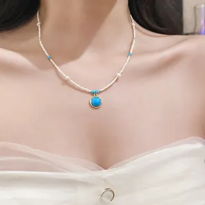Detailed shot of a vintage-style white beaded necklace with a round blue stone pendant.
