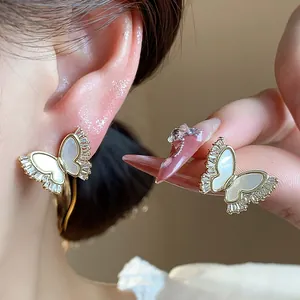 Macro detail of gold-plated butterfly earrings featuring sparkling zircons and shell inlays.